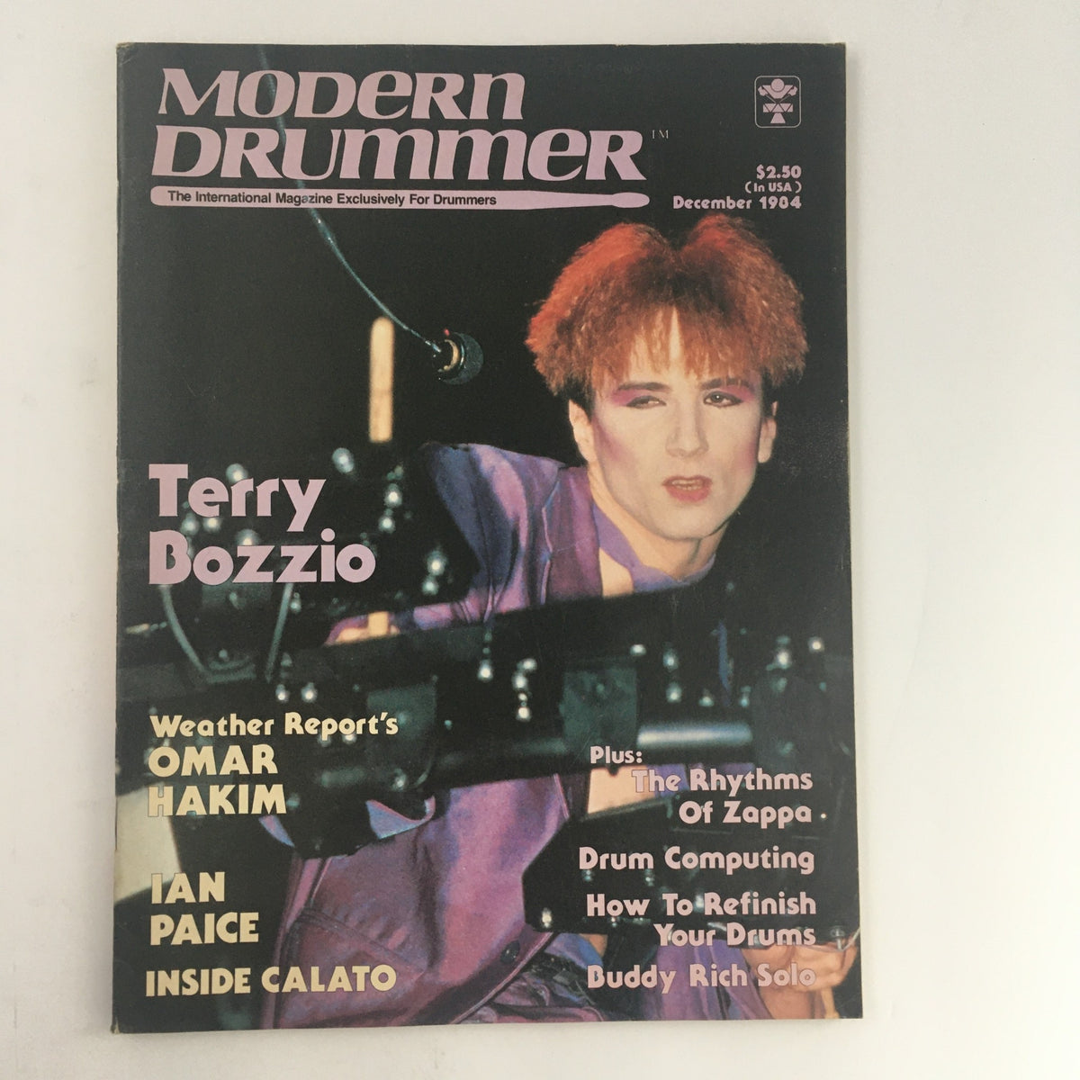 Modern Drummer Magazine December 1984 featuring drummers Terry Bozzio, Omar Hakim, and Ian Paice, showcasing music articles and interviews. The cover displays Terry Bozzio in performance attire with vibrant hair and an expressive face.