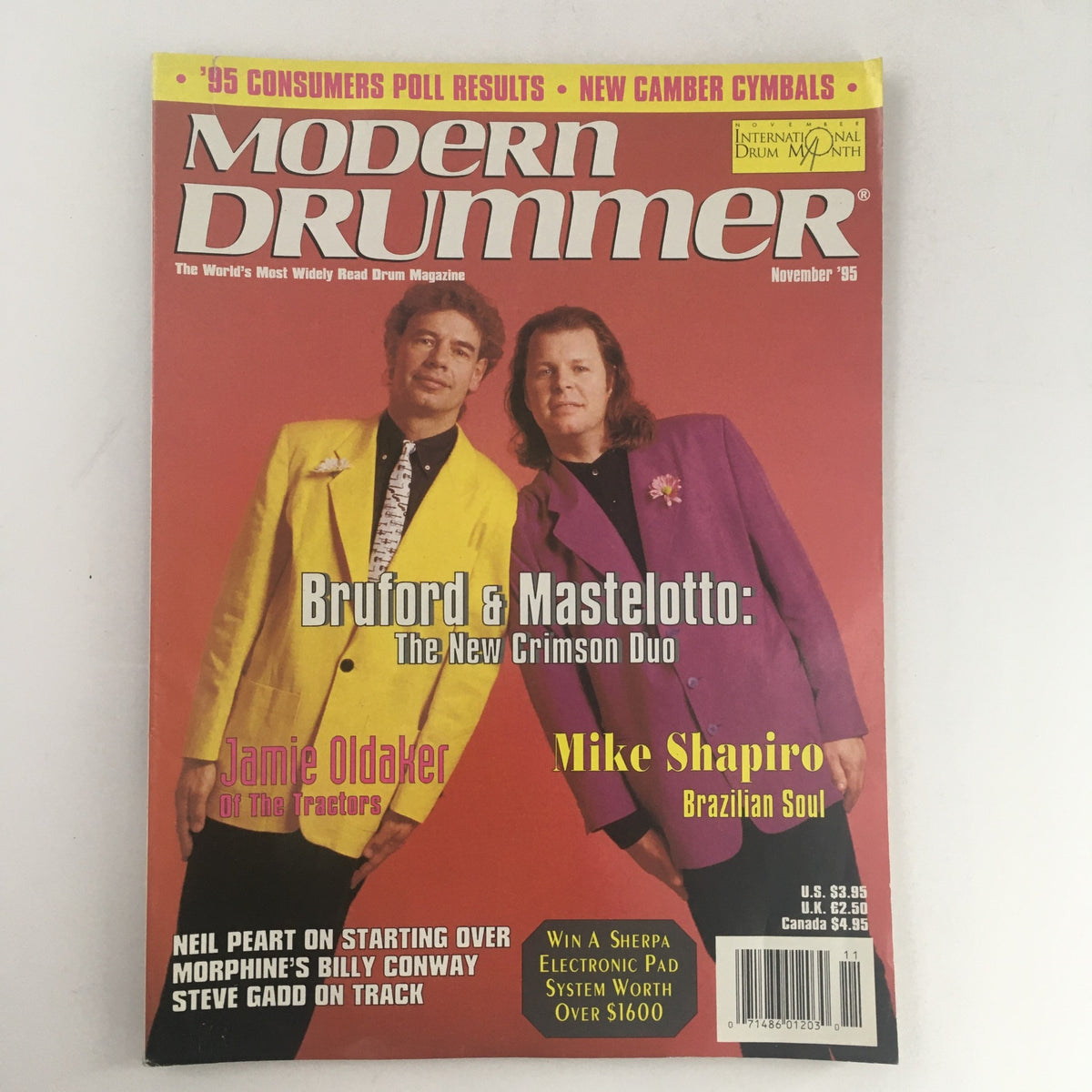 Cover of Modern Drummer Magazine from November 1995 featuring Bill Bruford and Pat Mastelotto, titled 'Bruford & Mastelotto: The New Crimson Duo'. The vibrant magazine showcases the duo in colorful suits against a red background, highlighting their influence in the drumming and progressive rock scene.
