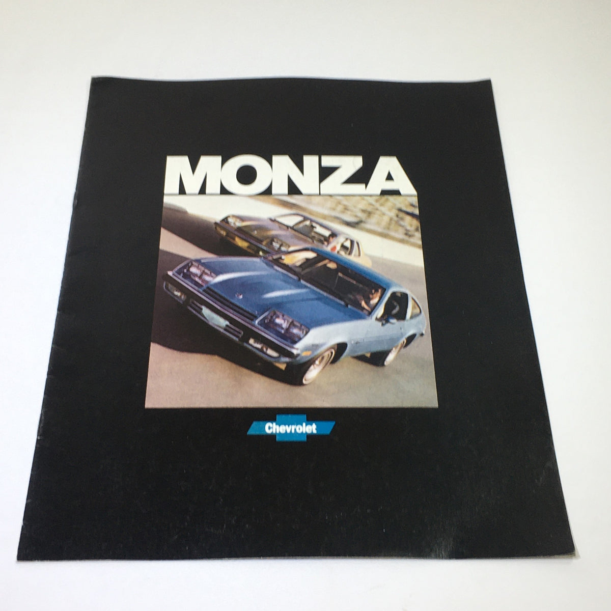 Cover of the September 1976 Chevrolet Monza Dealership Car Auto Brochure Catalog featuring a blue Chevrolet Monza on a racetrack background.