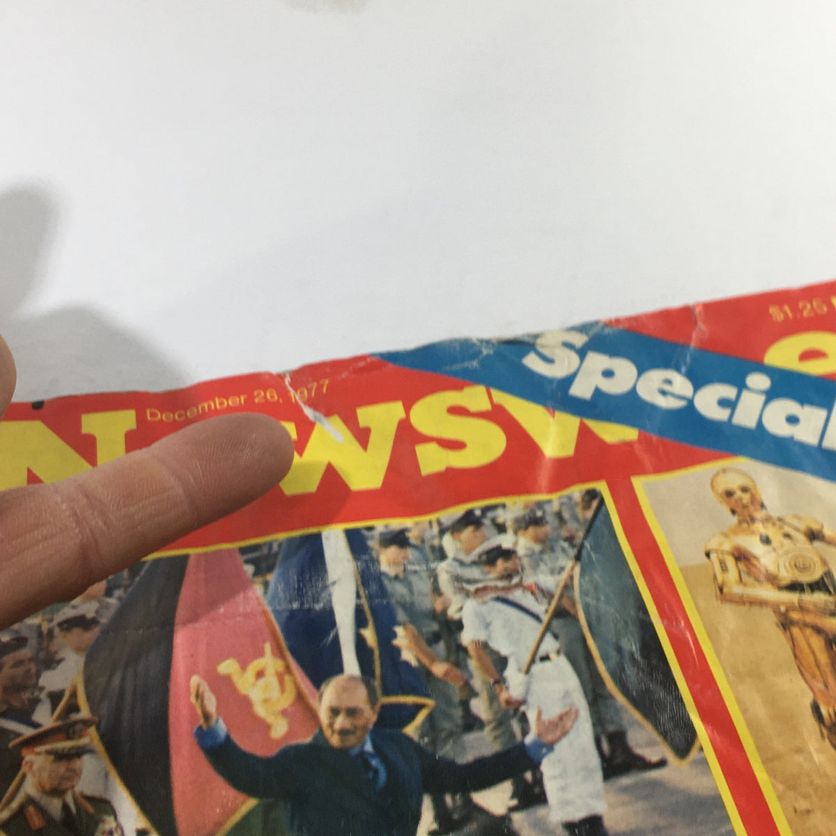 Close-up of Newsweek Magazine cover dated December 26, 1977, highlighting the title 'Pictures of 77'. A finger points towards a prominent historical figure being celebrated.