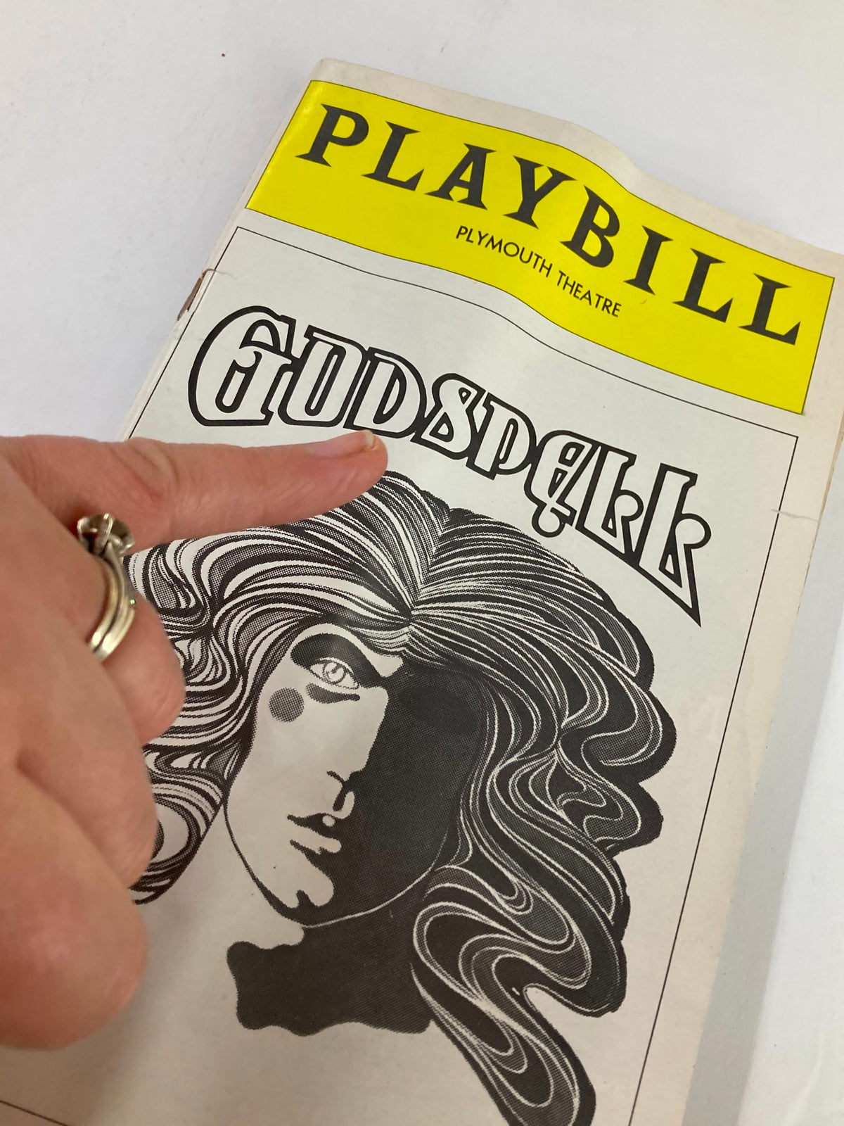 Close-up image of a 1976 Playbill from the Plymouth Theatre for Godspell, highlighting the cover design with playful character graphics and the title prominently displayed.