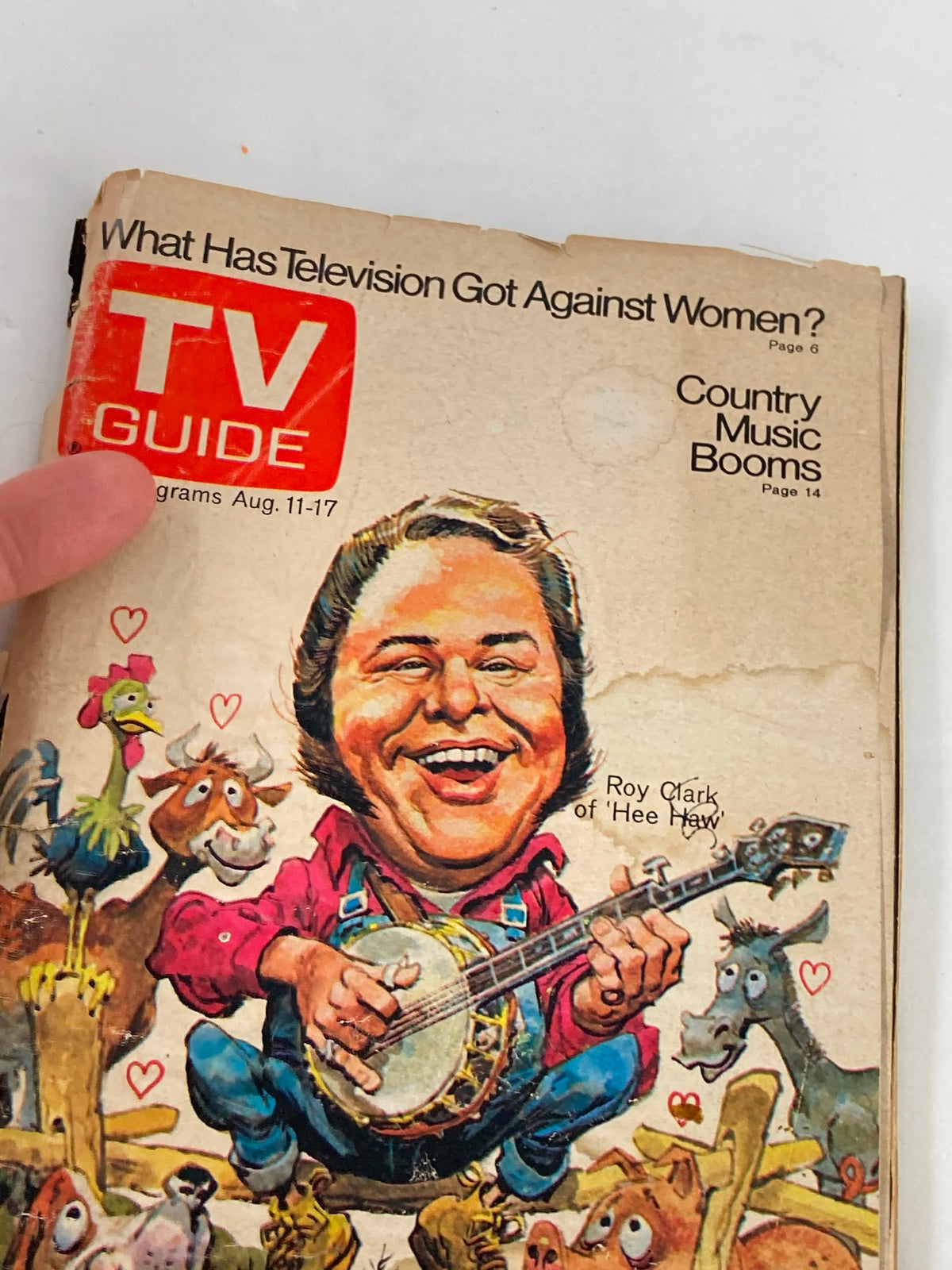Close-up view of the cover of TV Guide Magazine August 11 1973 #563 with Roy Clark's joyful illustration, highlighting the text 'What Has Television Got Against Women?' and various farm animals around him, emphasizing the magazine's nostalgic appeal.