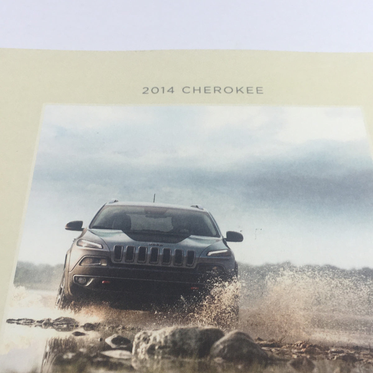 Close-up view of the 2014 Jeep Cherokee SUV Dealership Car Auto Brochure cover featuring a Jeep navigating through a splash, emphasizing its outdoor capability.