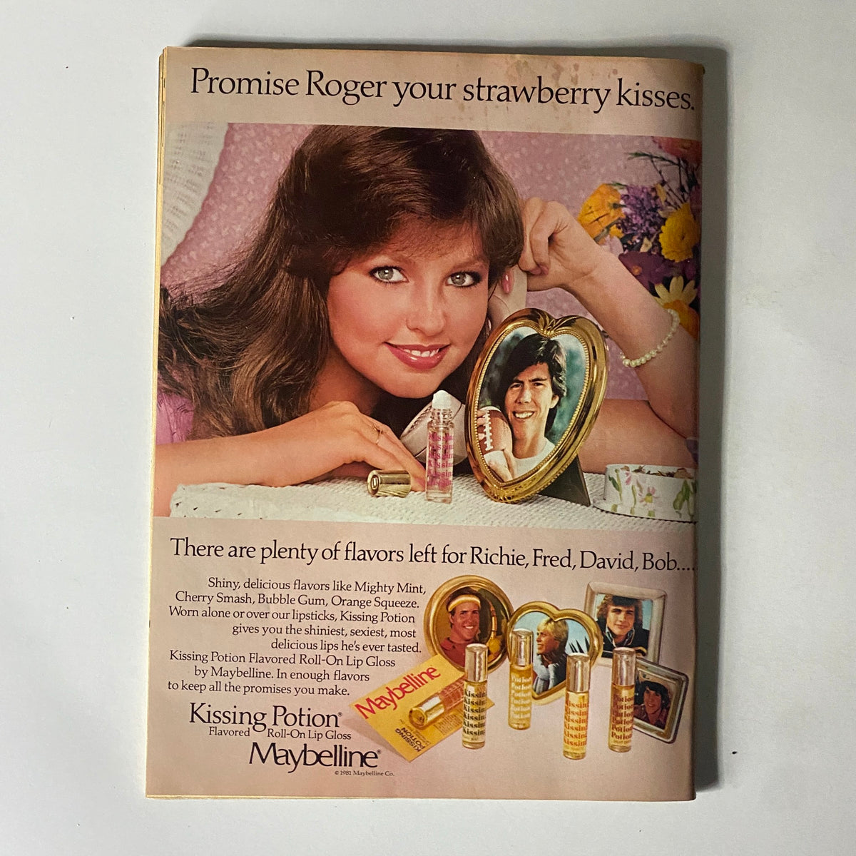 Advertisement from 16 Magazine December 1981 promoting Maybelline's Kissin' Potion lip gloss featuring a model and a heart-shaped photo frame.