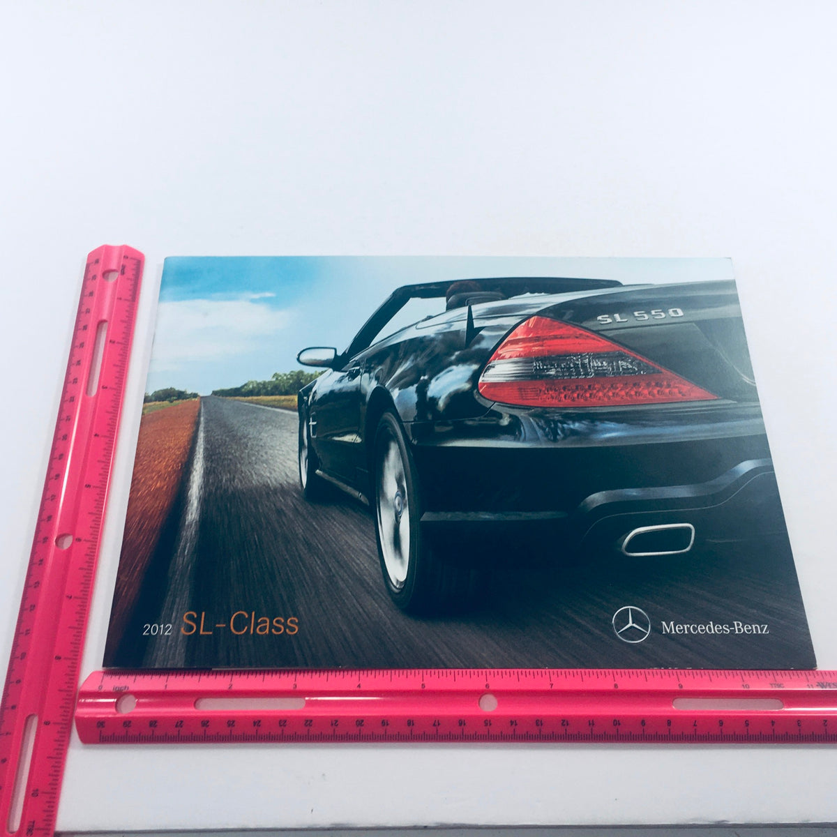 Cover image of the 2012 Mercedes-Benz SL-Class Dealership Car Auto Brochure Catalog displaying a black SL-Class 550 car on an open road with a ruler for scale.