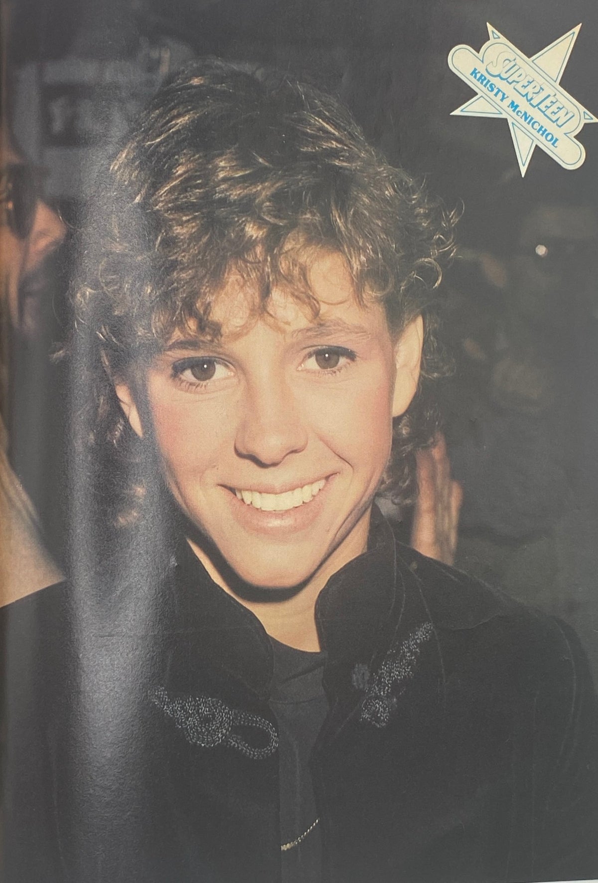 Close-up shot of a cheerful young boy with curly hair in a black outfit, smiling at the camera, as seen in SuperTeen Magazine November 1980, highlighting iconic teen stars of the era.