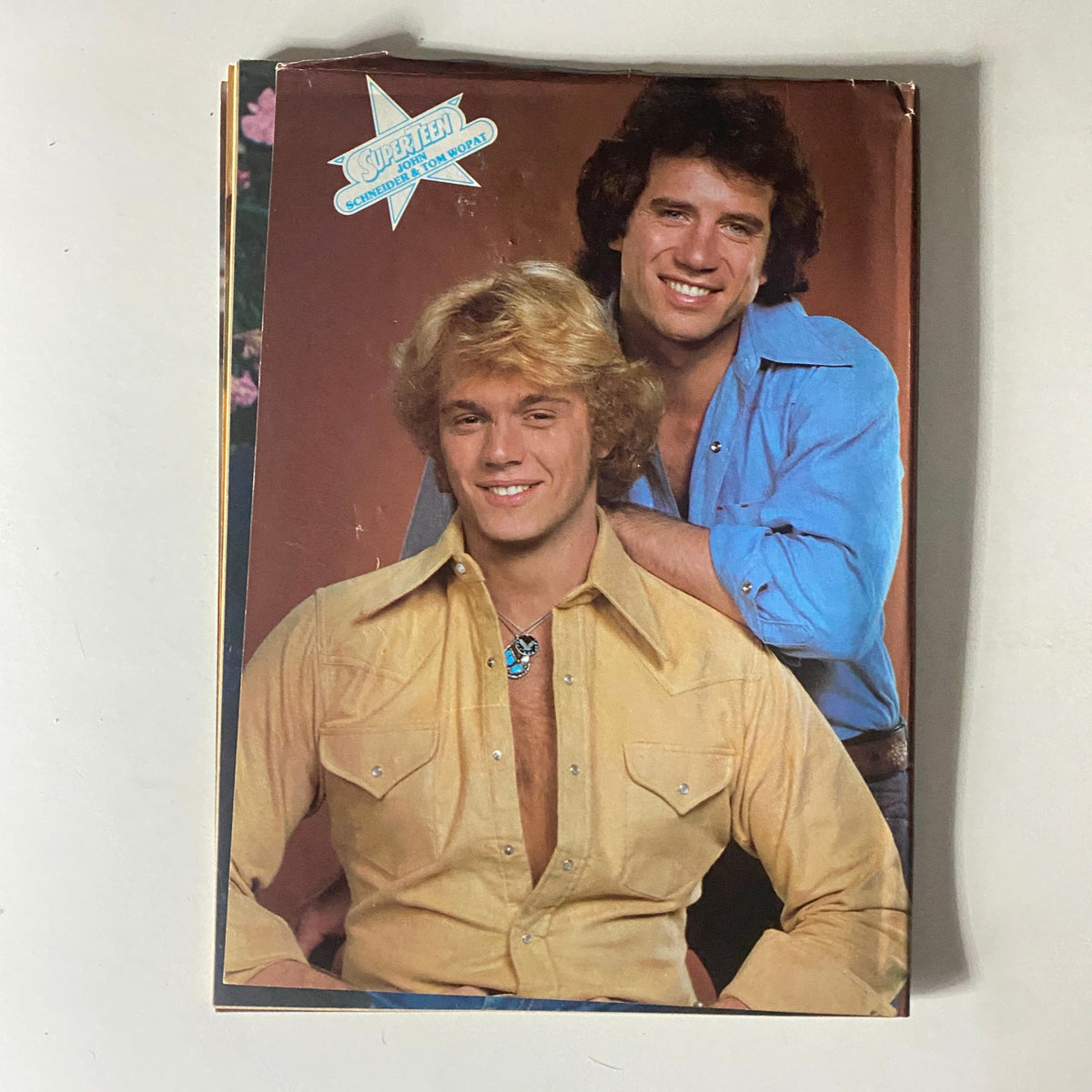 Studio photograph of two young male models, one with blond hair in a yellow shirt and the other with dark hair in a blue shirt, featured in SuperTeen Magazine November 1980, capturing the charm of 1980s celebrity culture.