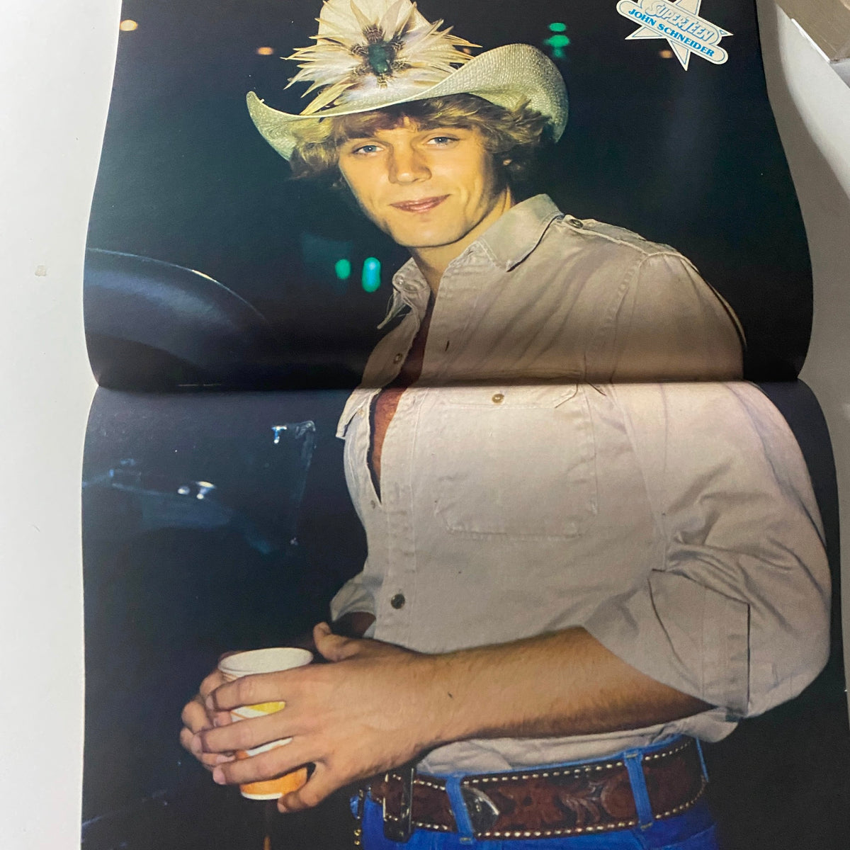 Blonde young man in a cowboy hat and shirt, confidently holding a drink, featured in SuperTeen Magazine June 1981.