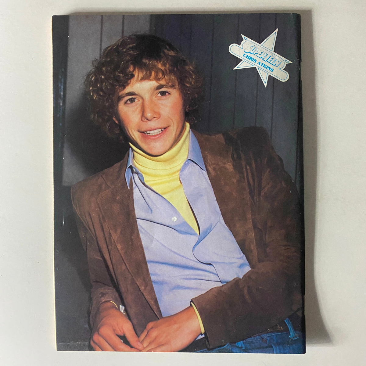Young man with curly hair in a brown jacket and yellow turtleneck, smiling for the camera in SuperTeen Magazine June 1981.
