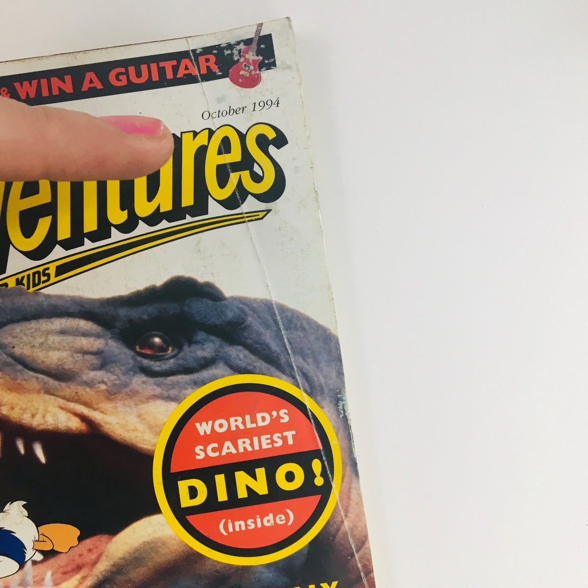 Close-up of the top section of Disney Adventures The Magazine, October 1994 issue showcasing the title and the tagline 'World's Scariest DINO!' with a guitar prize advertisement.