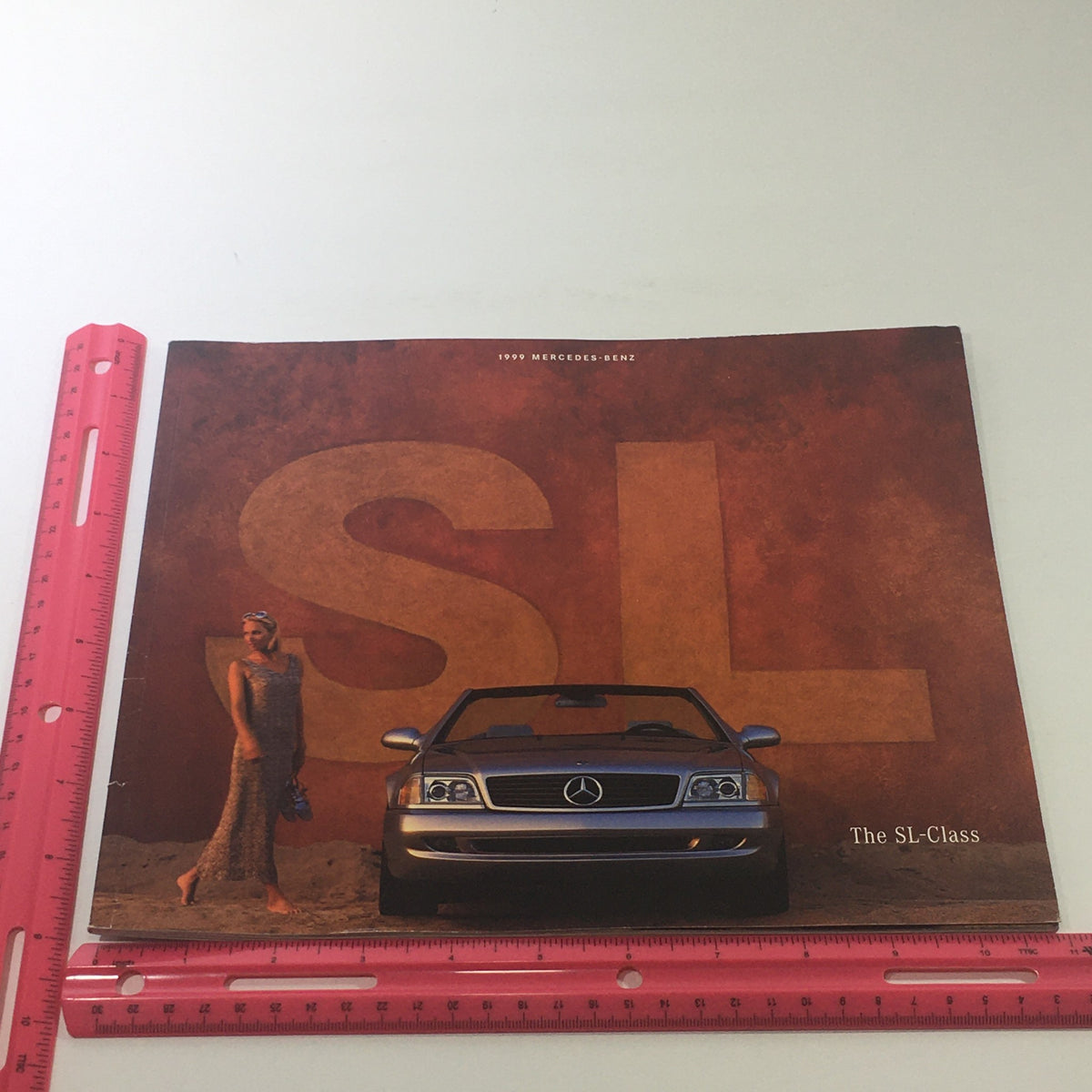 Front cover of the 1999 Mercedes-Benz SL-Class Sport Package Dealership Car Auto Brochure Catalog, highlighting the iconic car and a model against a textured backdrop.