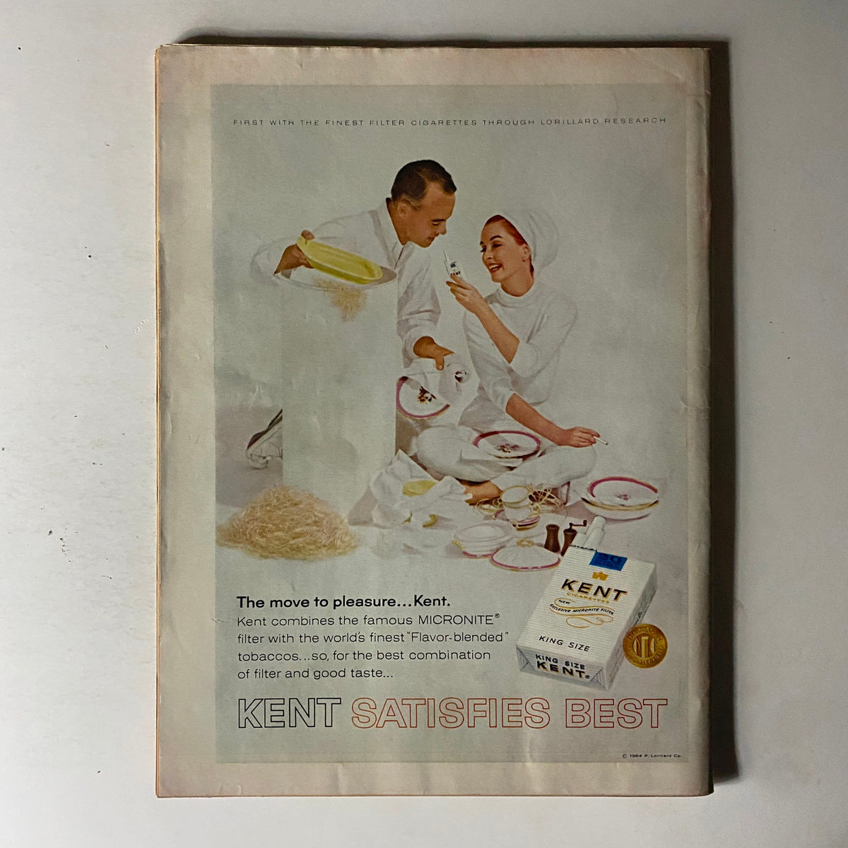 Vintage advertisement for Kent cigarettes, showcasing a couple in elegant attire engaging with porcelain tableware. This classic ad emphasizes the quality and flavor of Kent cigarettes, fitting into the lifestyle imagery of its time.