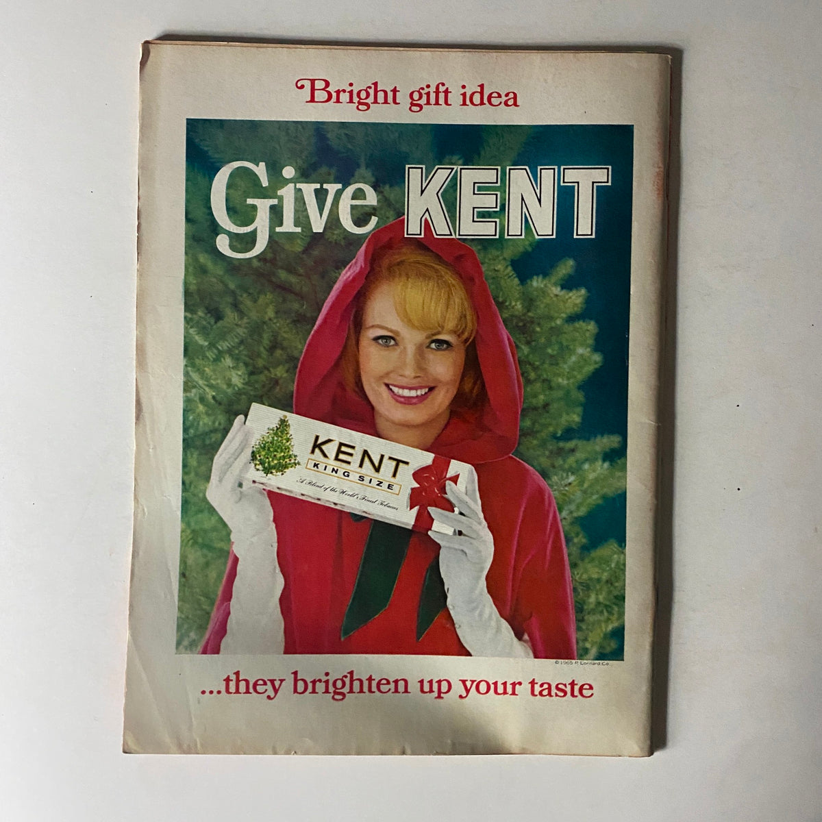 Vintage advertisement featuring a woman in a red hooded coat promoting 'KENT KING SIZE' cigarettes, with the caption 'Give KENT... they brighten up your taste,' set against a backdrop of Christmas greenery, from the Time Magazine December 24, 1965, Vol 86 No. 26, 'Rendezvous on the Road to the Moon.'