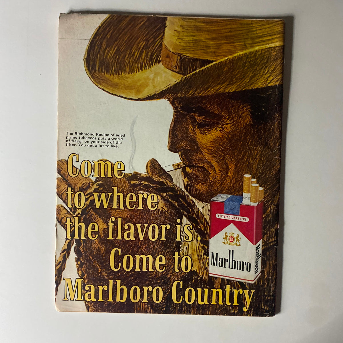 Vintage advertisement from 1965 promoting Marlboro cigarettes, showcasing a cowboy holding a cigarette and text inviting consumers to enjoy the flavor of Marlboro Country.
