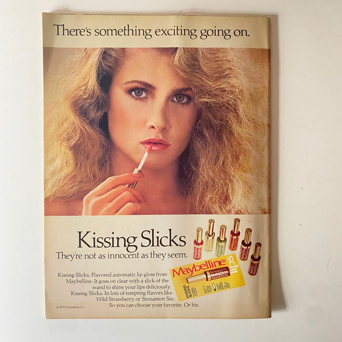 Maybelline advertisement featuring 'Kissing Slicks' lip gloss with a beautiful model applying lip gloss. The ad highlights the excitement of the product, mentioning flavors like Wild Strawberry and Cinnamon Sin. Part of the March 1981 issue of Teen Beat Magazine featuring John Schneider, Scott Baio, and Matt Dillon.