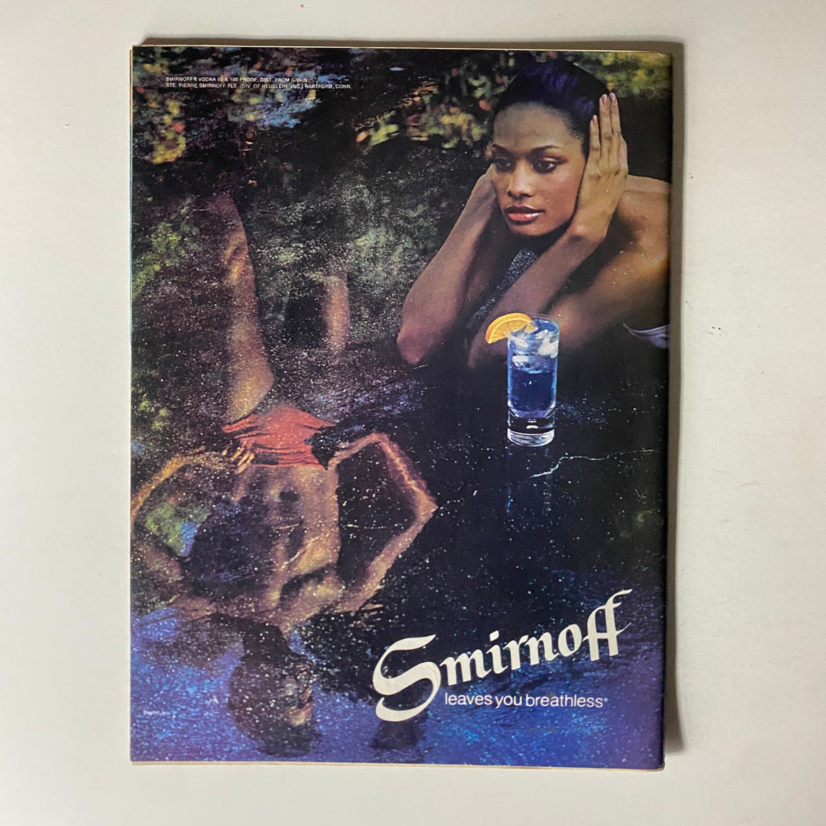Vintage advertisement featuring a model lounging by a pool, promoting Smirnoff's tagline 'leaves you breathless.' Includes a glass of drink, complementing the aesthetic of the Newsweek Magazine July 25, 1977 Blackout Special Color Report.