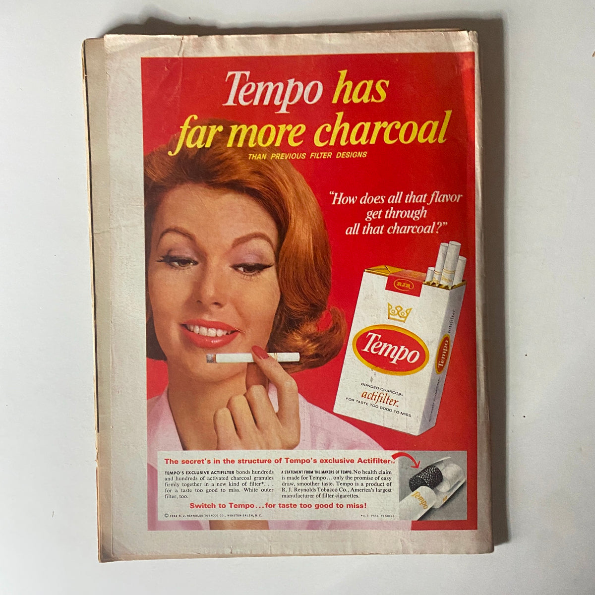 Vintage advertisement for Tempo cigarettes featuring a woman holding a cigarette and promoting the product's charcoal filter technology. The ad reads 'Tempo has far more charcoal than previous filter designs', showcasing the classic promotional style typical of mid-20th century marketing.