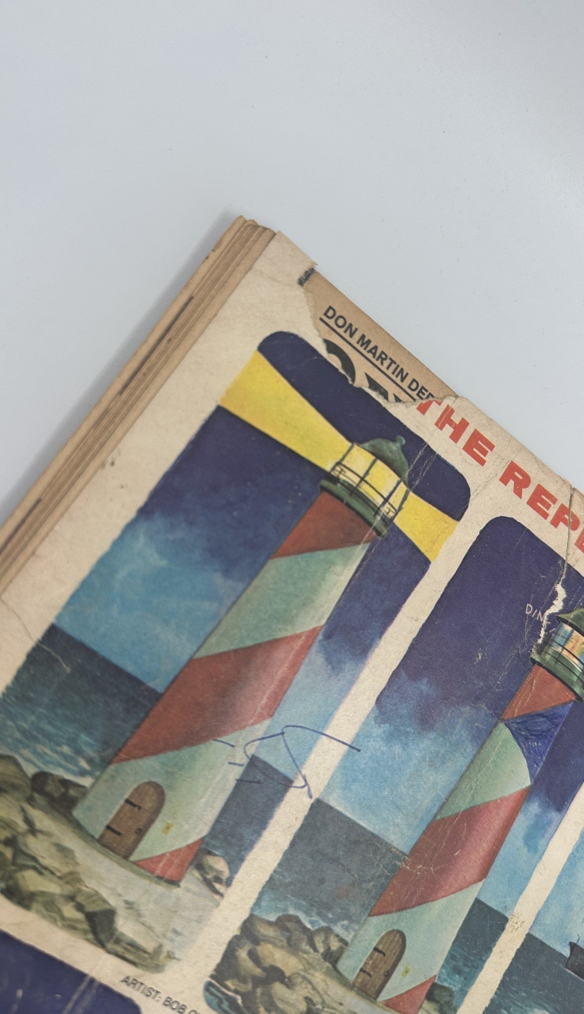 Cover detail of MAD Magazine No. 100, showing artwork by Bob Clarke featuring a lighthouse in a coastal scene, indicating damage with visible wear.