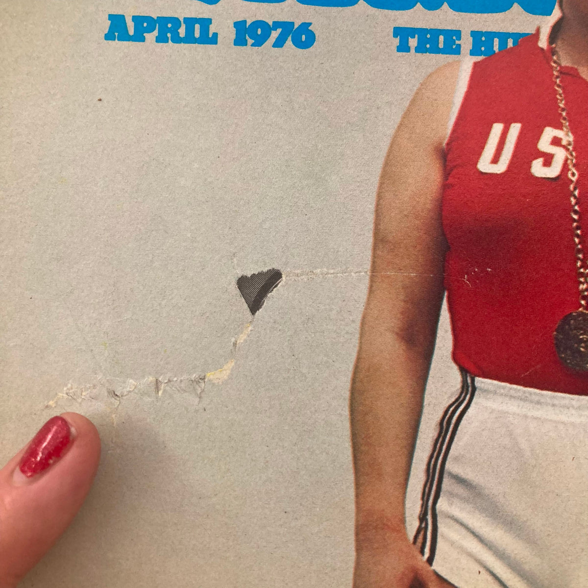 Close-up of the front cover of the Vintage National Lampoon Magazine from April 1976, featuring a damaged corner and a U.S. athlete wearing a medal.