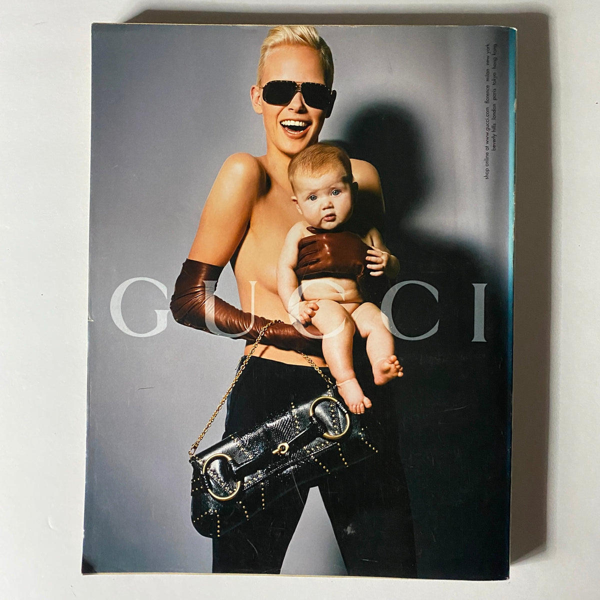 W Magazine October 2003 cover featuring a striking fashion photo of a model wearing sunglasses and holding a baby, presenting a bold Gucci fashion statement.