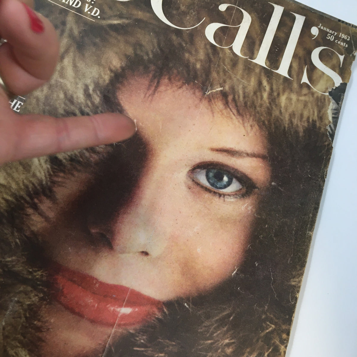 Close-up of the cover of VTG McCall's Magazine January 1963, showcasing a woman's face in a fur coat with a focus on her striking blue eye and red lips.