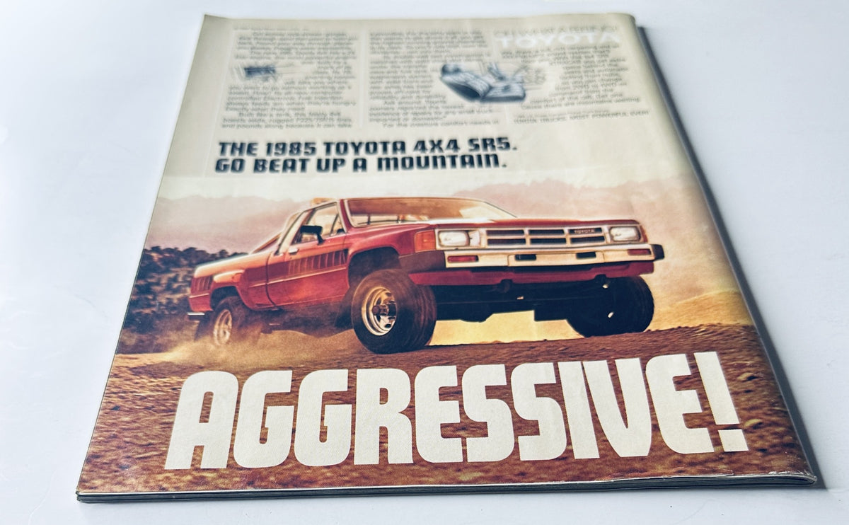 A second angle of the vintage advertisement for the 1985 Toyota 4x4 SR5 truck in Sports Illustrated Magazine December 10, 1984, showcasing its rugged exterior and the bold caption 'AGGRESSIVE!'