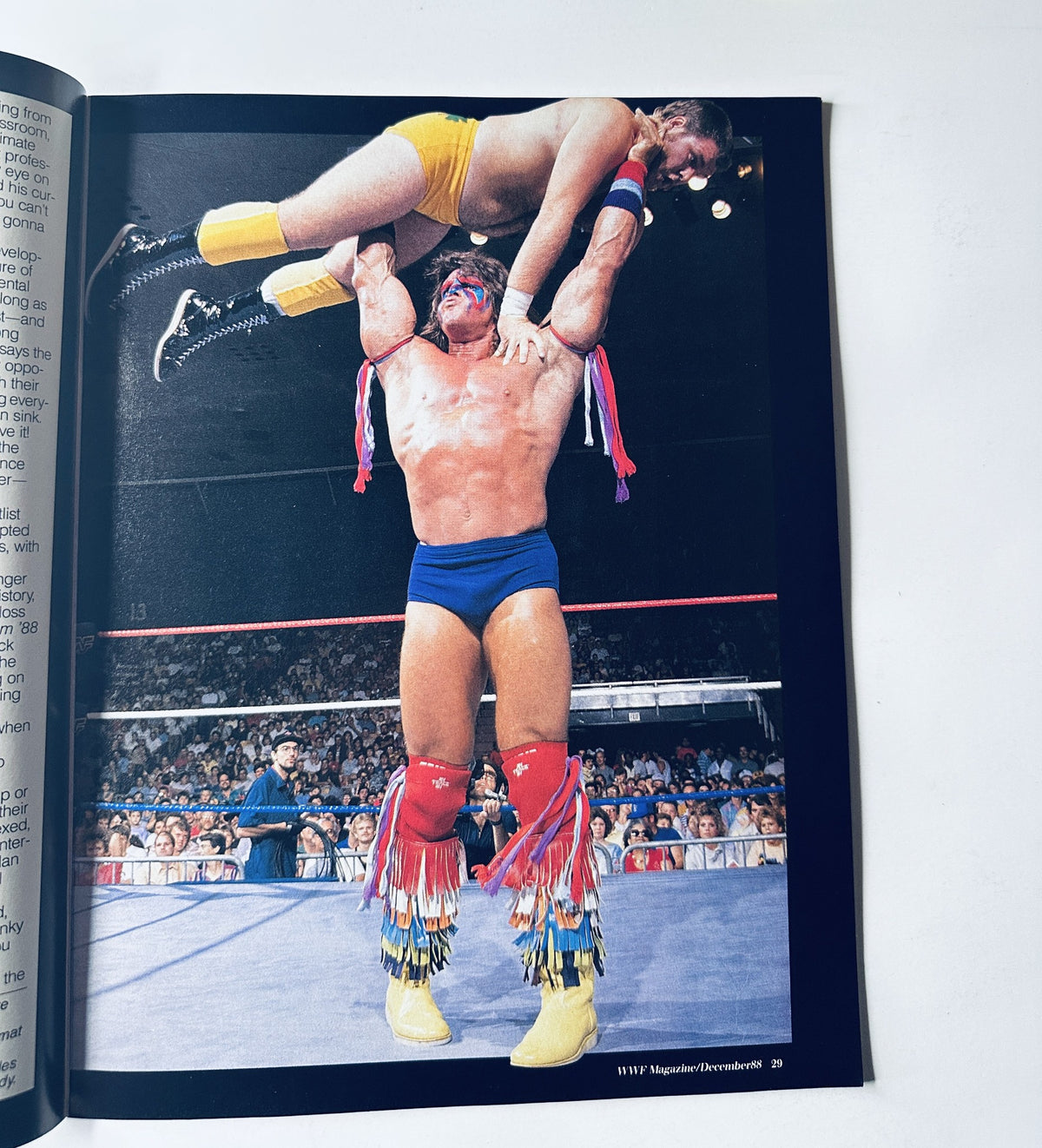 Action shot featured in WWF Magazine December 1988 showing The Ultimate Warrior lifting an opponent over his head in an intense wrestling match.