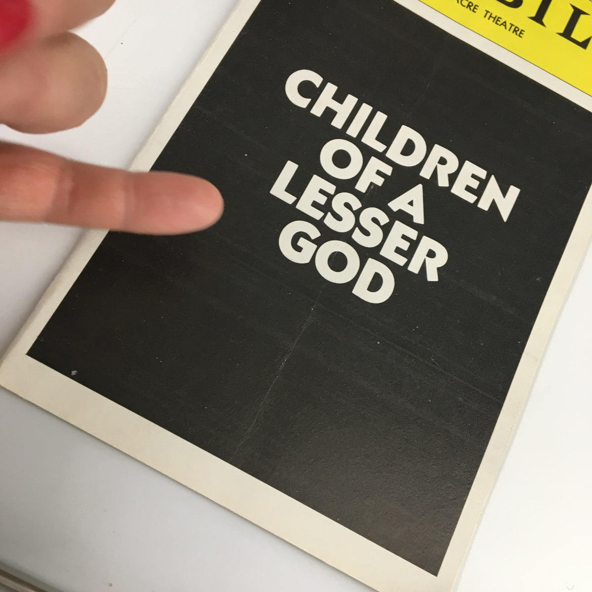 Close-up view of the 1980 Playbill for Children of a Lesser God, highlighting the title with a finger pointing.