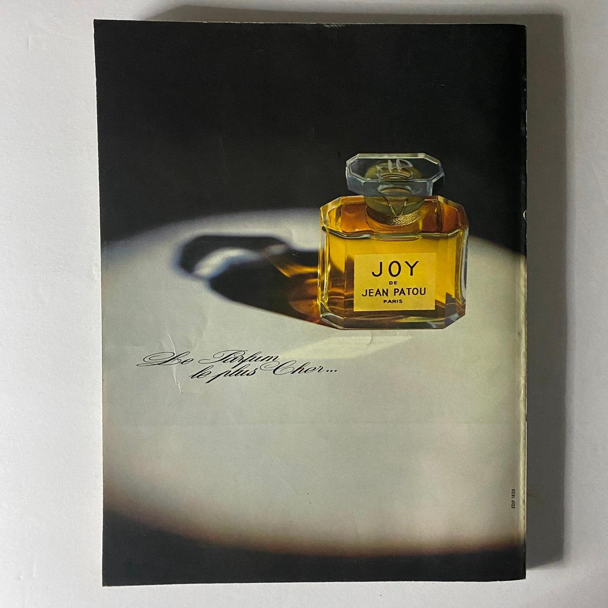 An elegant image of a classic perfume bottle labeled 'JOY de Jean Patou,' presented beautifully in the Vogue Paris Magazine March 1972. The sophisticated design emphasizes luxurious fragrance marketing from that era. Vogue Paris Magazine March 1972 Marie Laforêt Cover No Label VG.