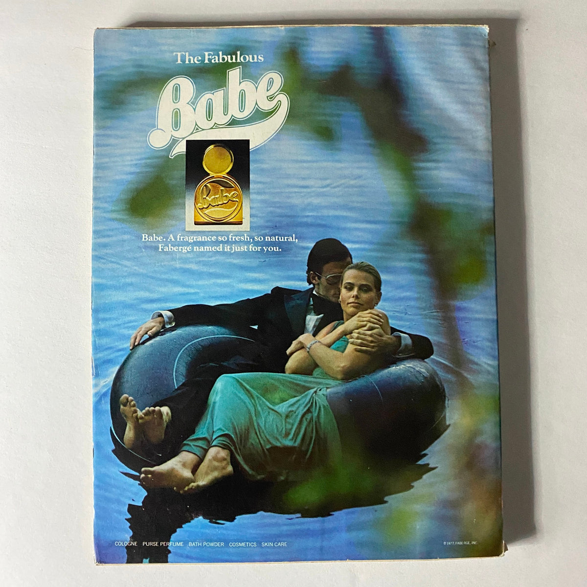Advertisement for Babe fragrance in Vogue Magazine December 1977, illustrating a couple relaxing on a river, capturing the essence of luxurious lifestyle and beauty.