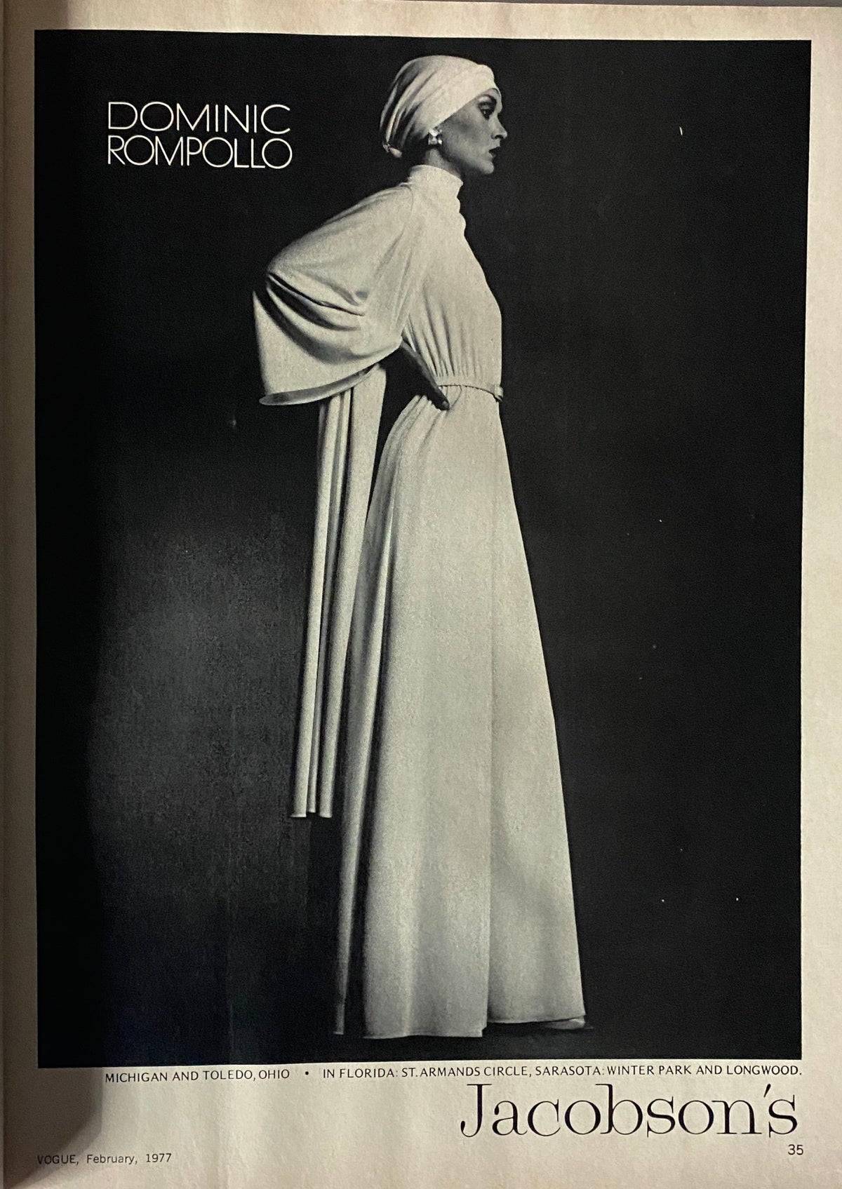 Black and white advertisement for Dominic Rompolo featured in Vogue Magazine February 1977, showcasing a stylish gown.