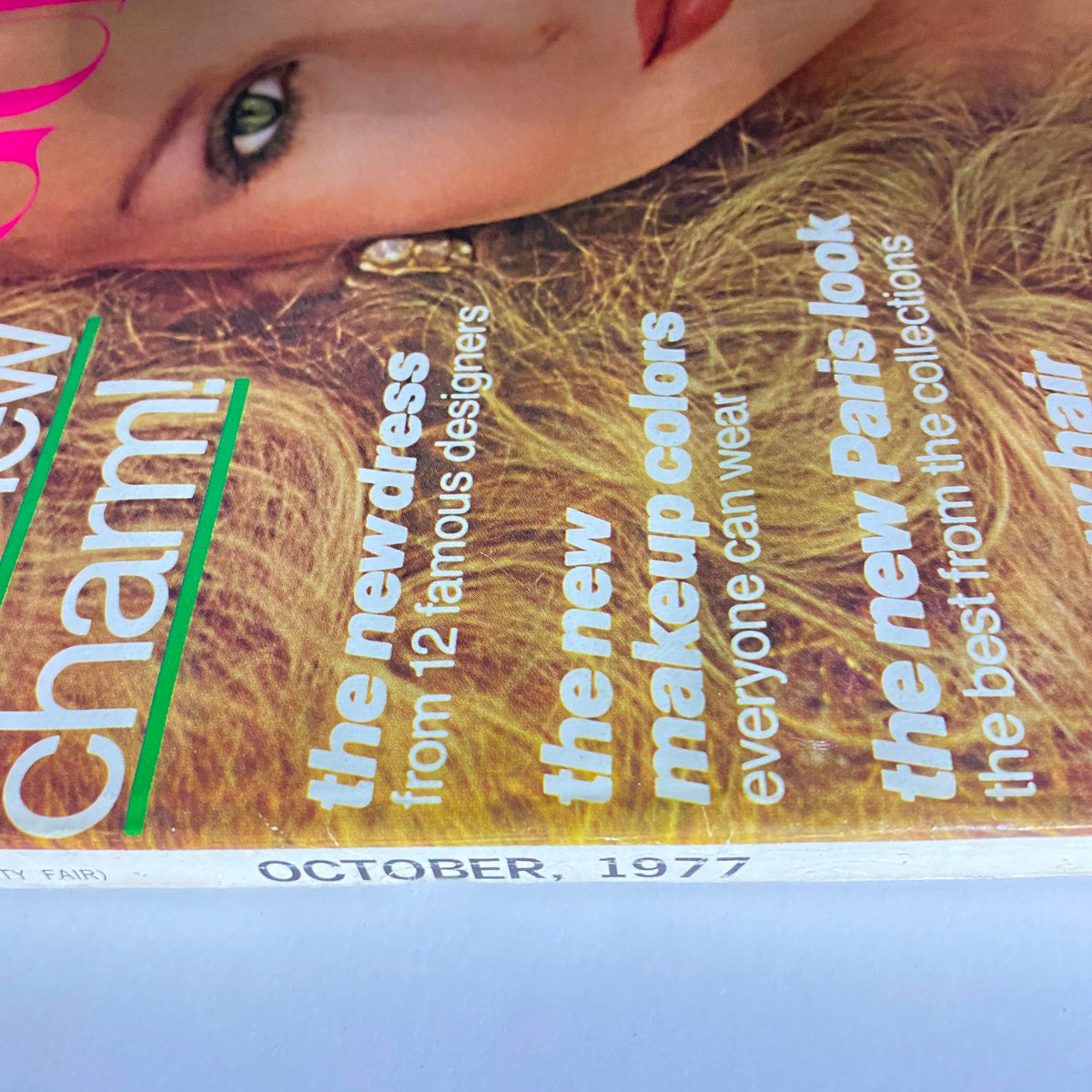 Close-up view of the Vogue Magazine October 1977 cover highlighting the phrase 'the new charm!' alongside features on fashion and makeup.