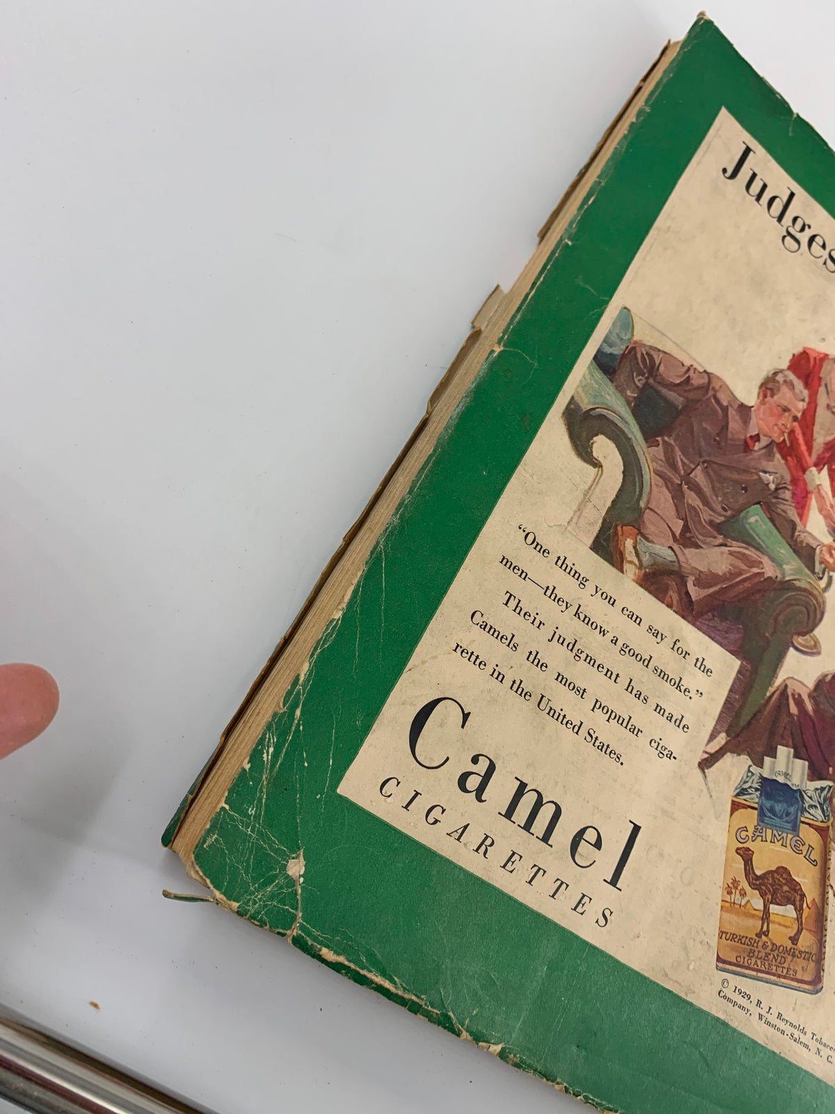 Close-up view of the side of the vintage December 1929 The American Mercury Magazine, showcasing the cover design featuring Camel Cigarettes and highlighting its wear and historic authenticity.