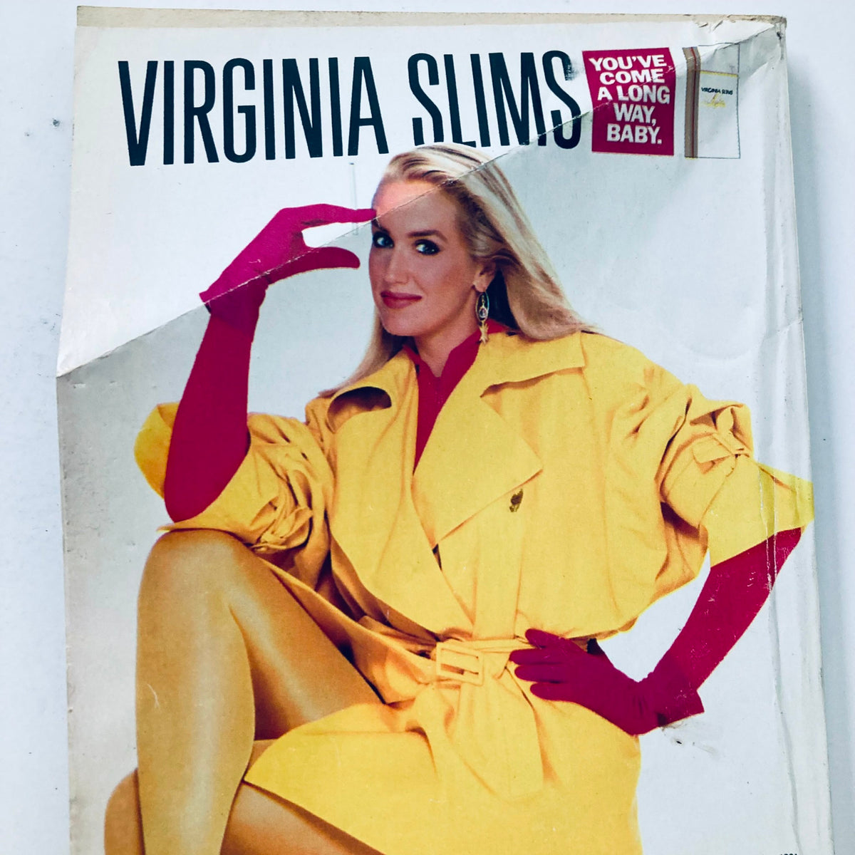 Virginia Slims advertisement featuring a glamorous model in a yellow coat and red gloves, illustrating fashion trends of the era.