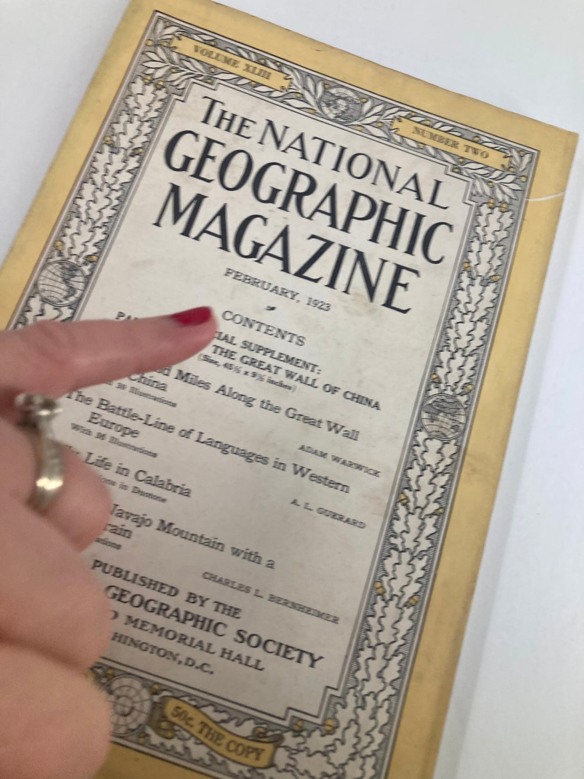 Close-up of the cover of The National Geographic Magazine, February 1923 edition, highlighting the title and contents list, with a finger pointing at the text.