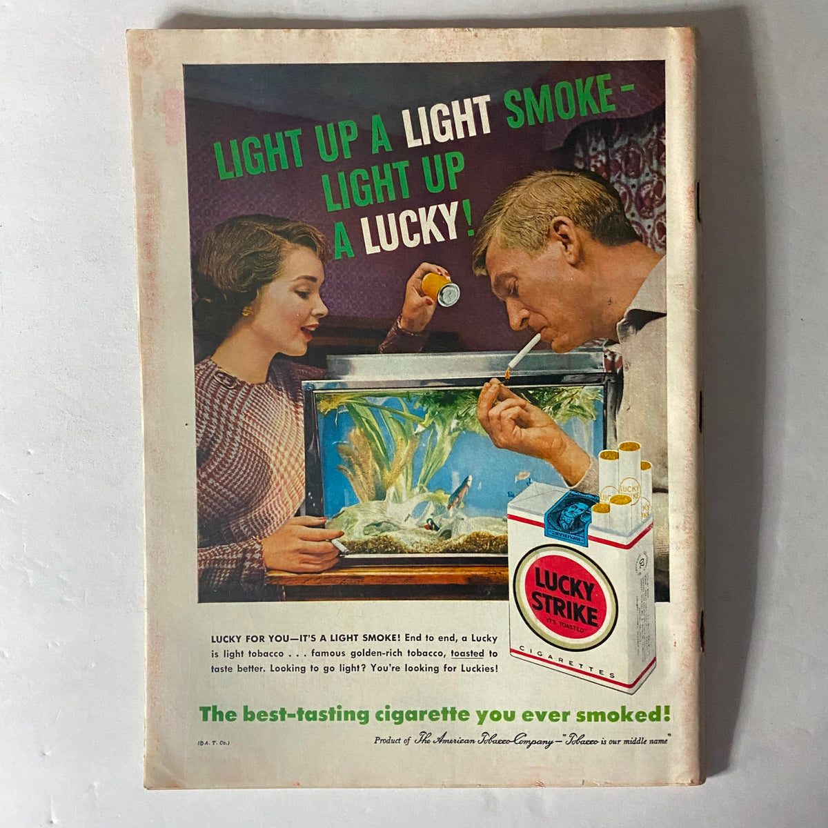 Vintage advertisement from a 1950s magazine with a couple near an aquarium promoting Lucky Strike cigarettes, highlighting mid-century marketing trends.