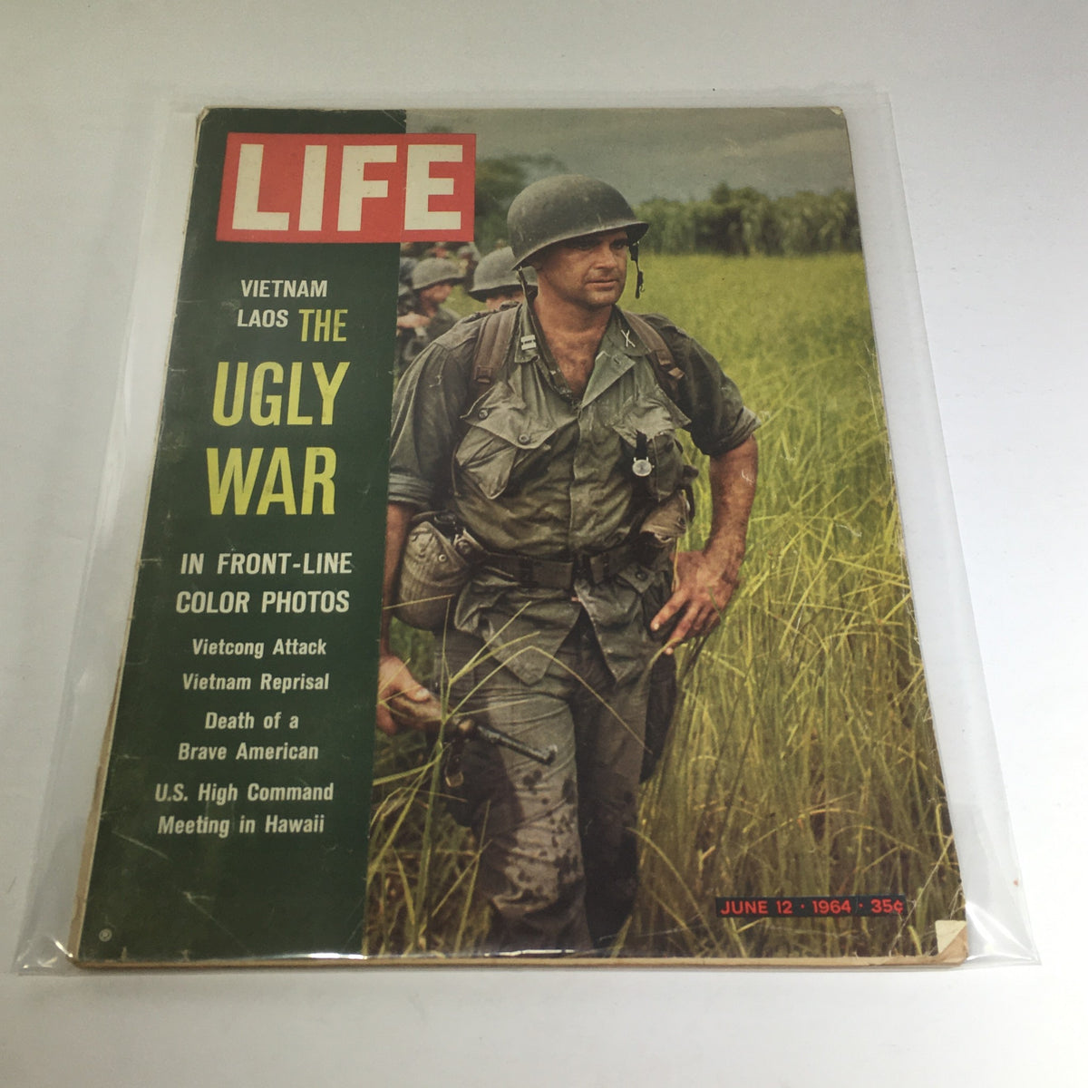 Cover of the VTG Life Magazine from June 12, 1964, titled 'Vietnam Laos The Ugly War in Front-Line Color Photos'. The cover showcases a soldier in a combat uniform walking through tall grass, highlighting the Vietnam War's harsh realities.