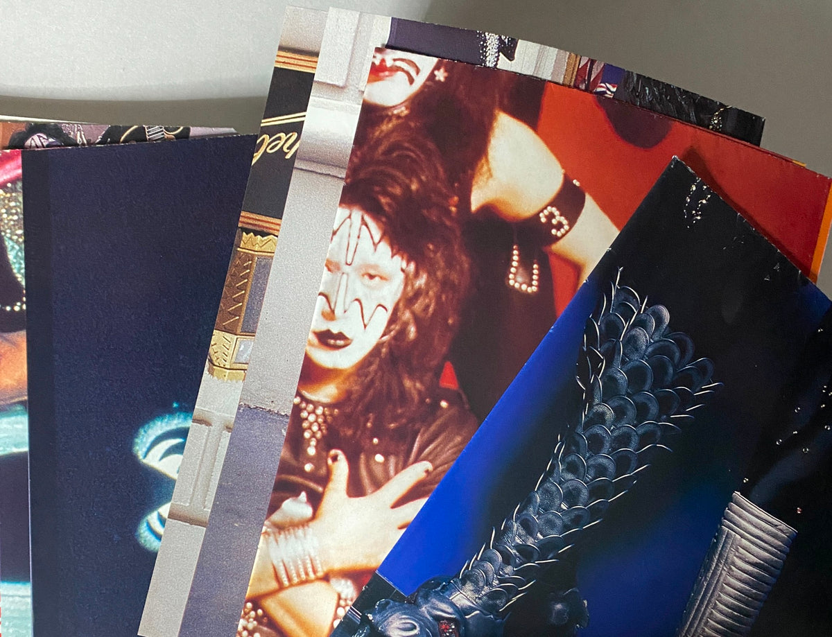 Collection of pages from the 2002 KISS: Hotter Than Hell: Stories Behind Every Song magazine by Paul Elliott, showcasing iconic imagery and artwork featuring KISS band members.