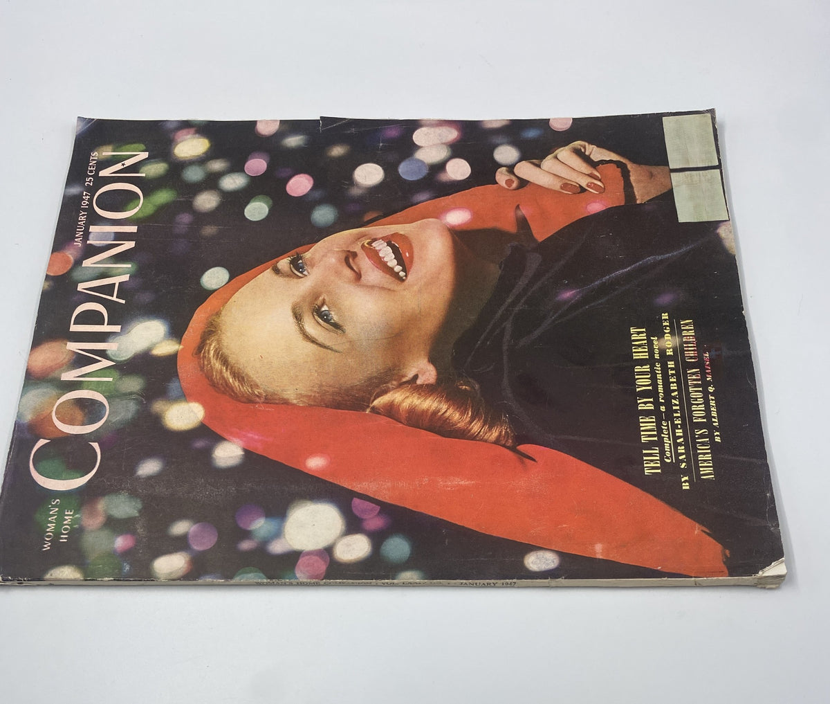 Woman’s Home Companion Magazine January 1947 cover showcasing 'Tell Time by Your Heart'. The image features a joyful woman in a red cape against a backdrop of festive bokeh lights, highlighting the magazine's vintage aesthetic.