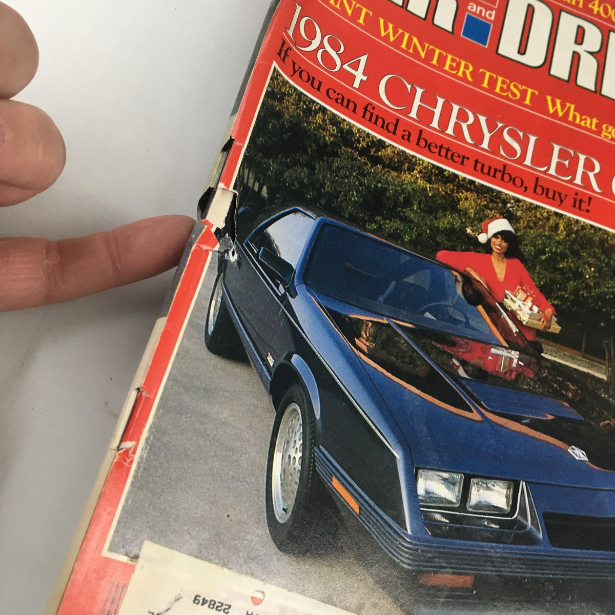 Close-up of Car and Driver Magazine December 1982 showing the 1984 Chrysler G24 cover; the image highlights wear on the magazine and the festive theme with a woman holding gifts.