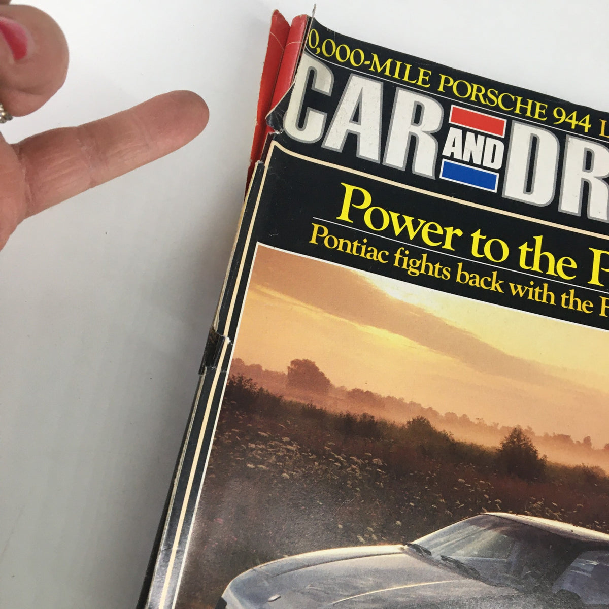 Close-up view of Car and Driver Magazine November 1984 highlighting the Pontiac Fiero GT V-6, with a finger pointing towards the cover headline.