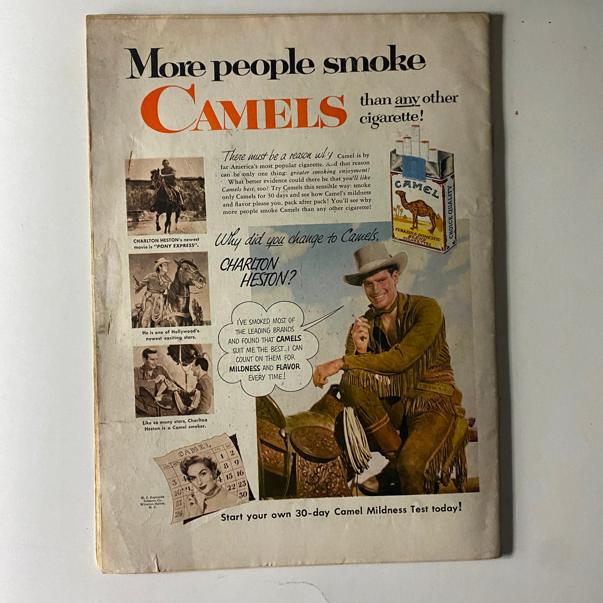Vintage advertisement for Camel cigarettes featuring Charlton Heston, promoting the slogan 'More people smoke Camels than any other cigarette!'. Highlights a question to Heston about his choice of cigarette brand and showcases images of him in cowboy attire, indicative of the Western genre.