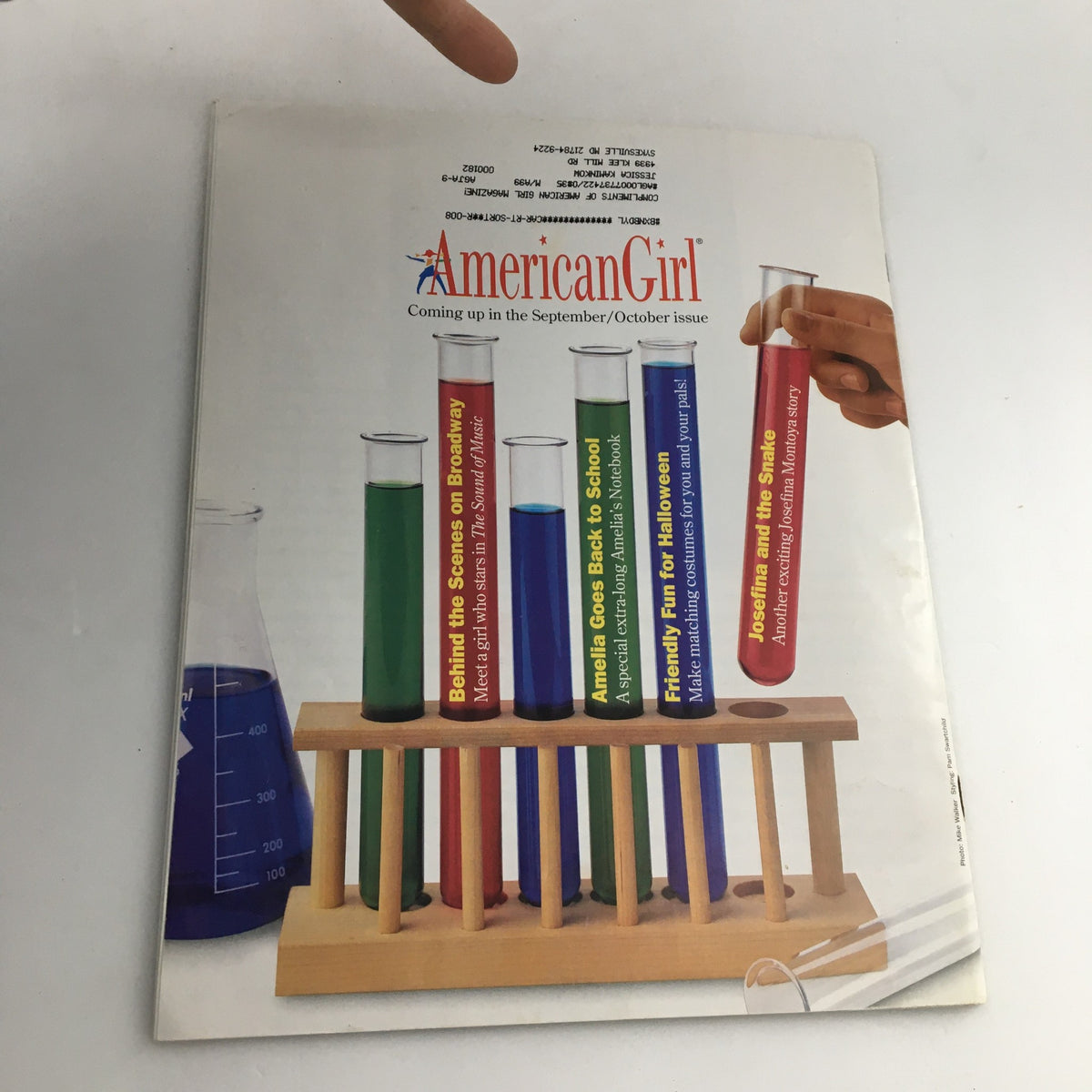 Cover of American Girl Magazine July-August 1998 featuring a display of colorful test tubes with titles related to upcoming articles, including 'Behind the Scenes on Broadway' and 'Amelia Goes Back to School'.