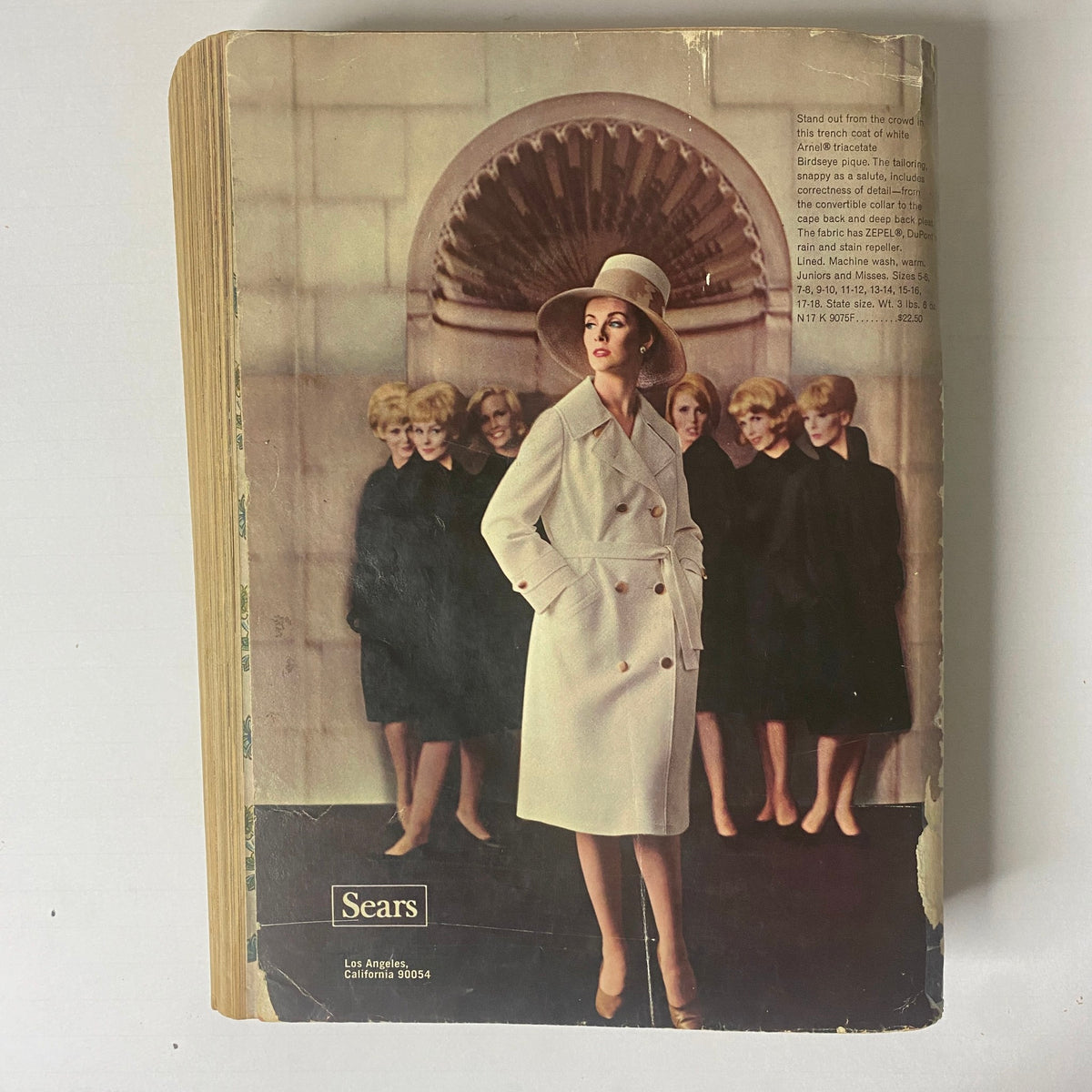 Cover illustration of the 1964 Sears Mr. John Classic Hats Spring - Summer Catalog featuring a model wearing an elegant hat and coat ensemble in a fashionable setting.