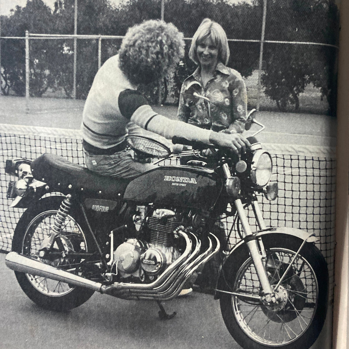 A retro image from Cycle World Magazine July 1976 showing a man on a Honda motorcycle interacting with a woman, representing the motorcycle culture of the 1970s.
