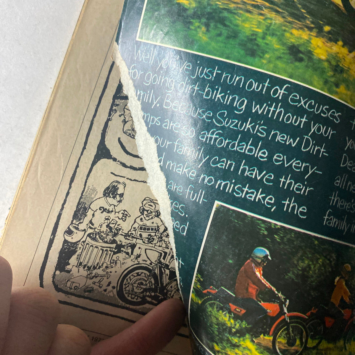 Inside page of Cycle Guide Magazine July 1977, displaying a torn section revealing text about Suzuki Dirt-Scamps and a cartoon illustration.