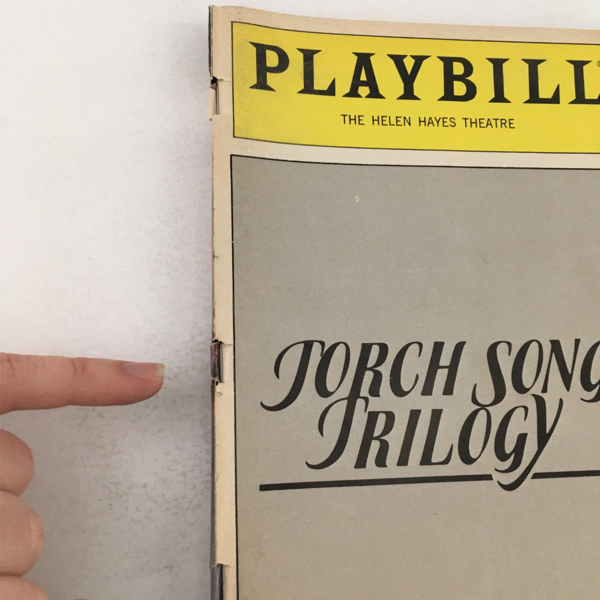 Close-up view of the 1983 Playbill for 'Torch Song Trilogy' showing the iconic title, emphasizing its vintage design from The Helen Hayes Theatre.