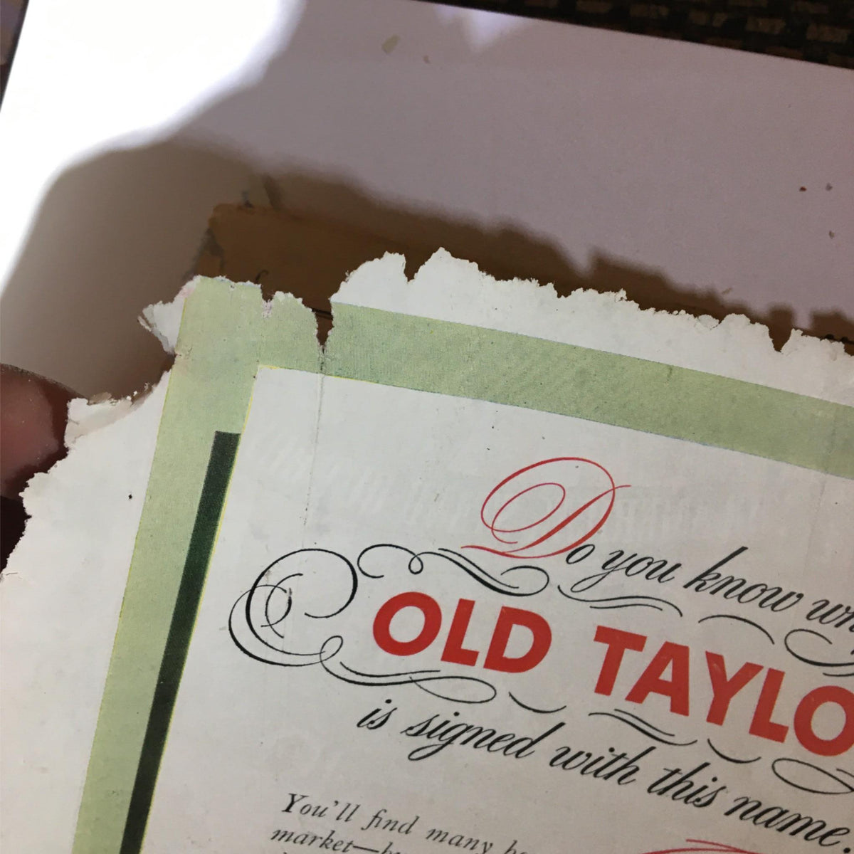 Close-up of the torn edge of an advertisement for Old Taylor Bourbon, dated 1940, showcasing vintage design elements and condition details.