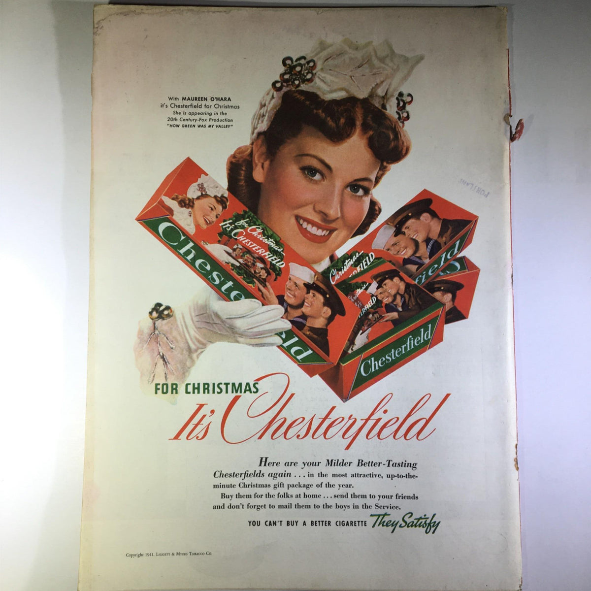 Vintage advertisement featuring a smiling woman with red lipstick and a white glove, promoting 'Chesterfield' cigarettes for Christmas. The advertisement includes colorful packages of Chesterfield cigarettes, making it a historical piece from the 1940s. This image emphasizes the cheerful holiday theme in the context of the era during World War II.