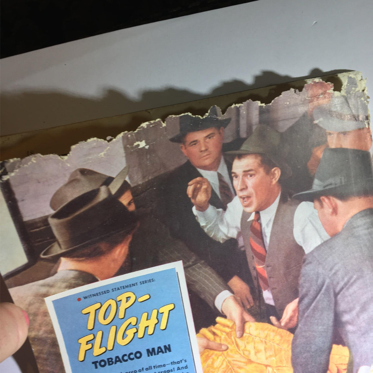 Back cover of an old magazine with a colorful illustration and damage showing jagged edges, related to the Newsweek Magazine July 17, 1939, depicting scenes related to 'Top-Flight Tobacco Man'.